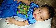Elijah joined the competition — help win amazing prizes! baby, sleeping, child, blue_clothing, pillow, couch, face, hand, peaceful, indoors, toddler, curly_hair, relaxed, portrait, infant, cute, cartoon_tshirt, resting, young_child, casual