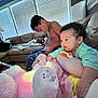 Kinsley is registered to the contest to win money with this photo: baby, child, living_room, sofa, plush_toy, pajamas, window_blinds, lamp, blanket, couch, smiling, curly_hair, toy, indoor, family, relaxing, person, sitting, device, casual