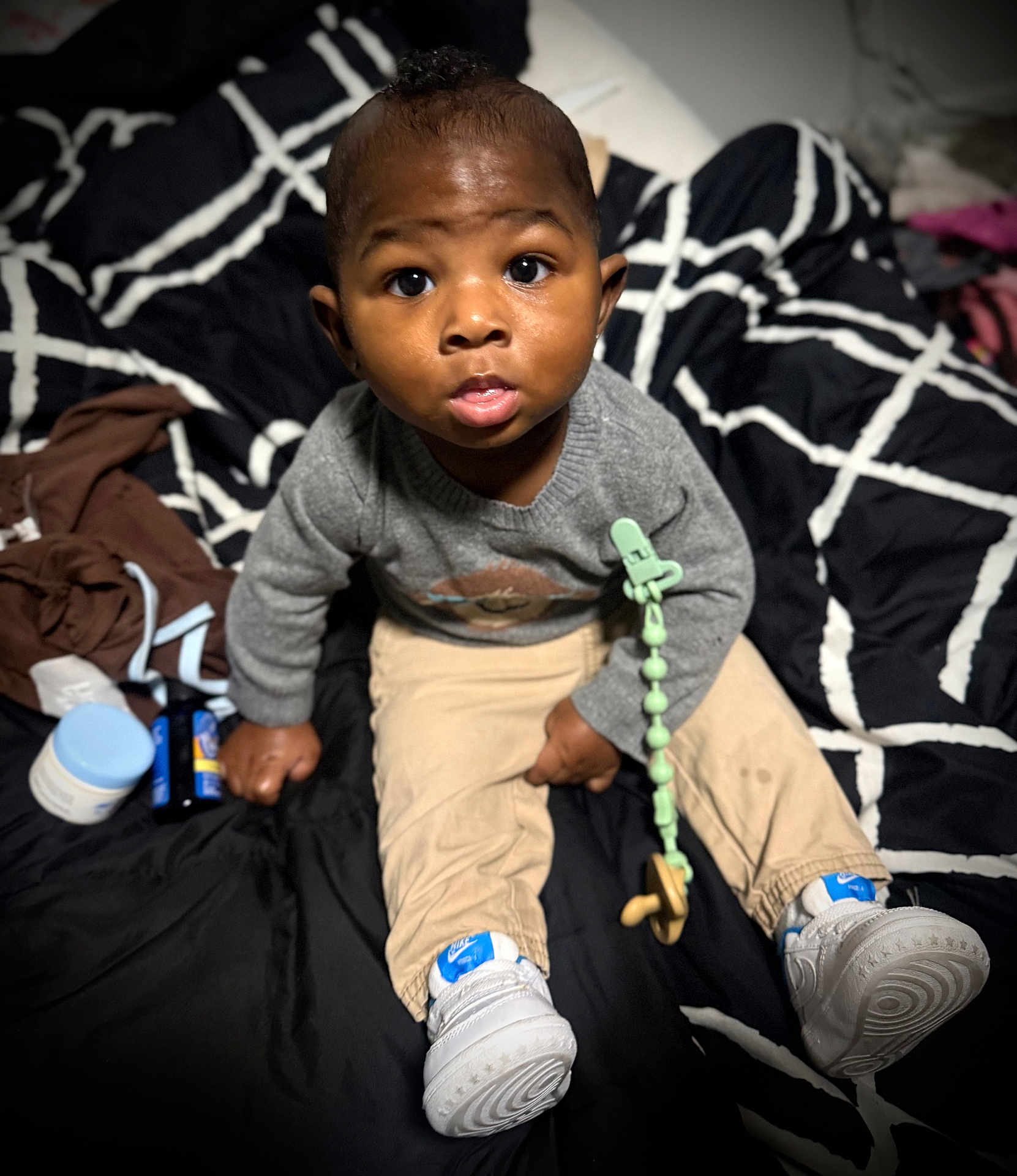 Zavon is registered to the contest to win money with this photo: toddler, child, infant, baby, sitting, indoors, clothing, sweater, pants, sneakers, pacifier, blanket, pattern, expression, face, curious, human, person, toy