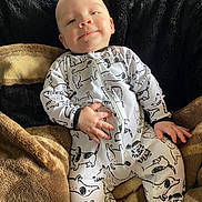Damon joined the competition — help win amazing prizes! baby, infant, smile, onesie, dog_pattern, blanket, cozy, indoors, child, cute, happy, relaxed, portrait, hand, face, sitting, soft_texture, warm, young_child, clothing