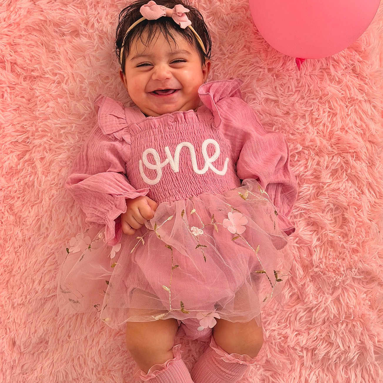 Ammarah is registered to the contest to win money with this photo: baby, child, pink, balloon, smile, dress, headband, sock, fluffy_rug, happy, portrait, one_year_old, cute, infant, lying_down, celebration, soft_texture, toddler, person, fun