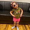 child, toddler, sunglasses, heart_shaped, pink_bow, green_shirt, pink_shorts, socks, wooden_floor, leather_couch, indoor, standing, posing, happy, cute, fashion, smiling, person, casual, playful