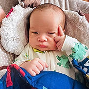 Josue is registered to the contest to win money with this photo: baby, infant, blanket, onesie, frog_pattern, hand, face, expression, indoors, wood_floor, pillow, sleepwear, cute, child, portrait, cozy, fingertip, resting, bedding, thoughtful