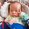 baby, infant, blanket, onesie, frog_pattern, hand, face, expression, indoors, wood_floor, pillow, sleepwear, cute, child, portrait, cozy, fingertip, resting, bedding, thoughtful