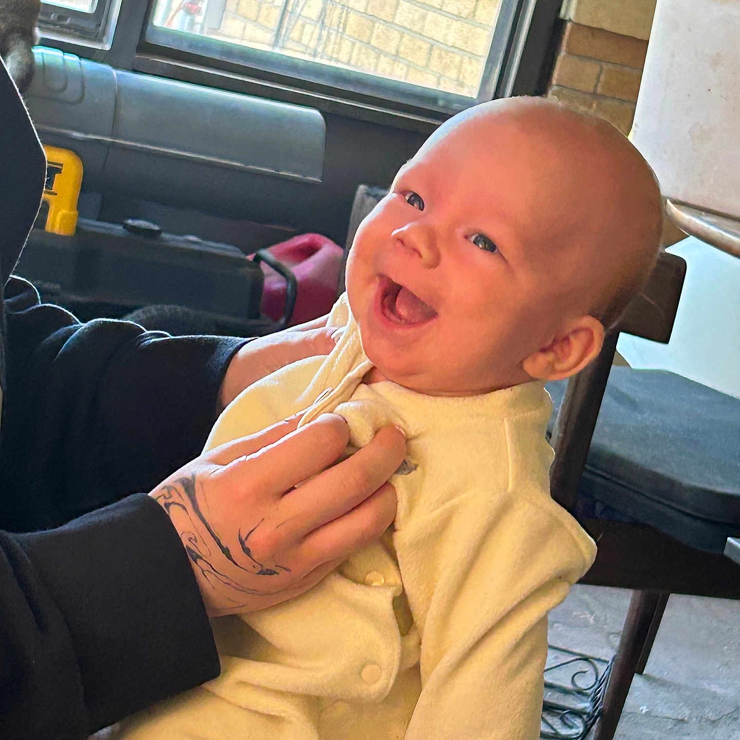 Augi is registered to the contest to win money with this photo: baby, candid, chair, clothing, cozy, cute, face, furniture, hand, happy, holding, indoor, infant, light, person, portrait, sleeve, smiling, tattoo, window