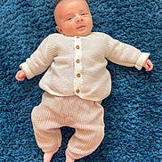 Roméo participe au concours pour gagner de l'argent avec cette photo : baby, infant, knitwear, beige_clothing, blue_carpet, lying_down, cute, face, small_feet, buttoned_sweater, long_sleeves, soft_texture, indoors, child, portrait, cozy, newborn, expression, person, casual