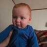 baby, infant, child, portrait, blue_outfit, sitting, face, eyes, looking_away, indoor, home, couch, blanket, adult_hand, support, close_up, soft_lighting, short_hair, calm, photography