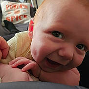 Erik is registered to the contest to win money with this photo: baby, infant, child, smiling, portrait, close_up, face, eyes, hands, adult_hand, car, car_seat, pillow, pumpkin_spice, indoor, sitting, casual, clothing, happy, road_trip