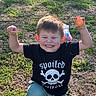 child, boy, smile, happy, outdoor, grass, egg, black_tshirt, skull_design, green_pants, sunlight, playful, kneeling, person, nature, casual_clothing, fun, youth, expression, celebration