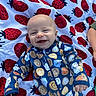 Brayden is registered to the contest to win money with this photo: baby, smiling, infant, blanket, strawberry_pattern, onesie, clothing, cute, happy, face, head, child, person, lying_down, pattern, food_illustration, milk_carton, cookie, outdoor, colorful