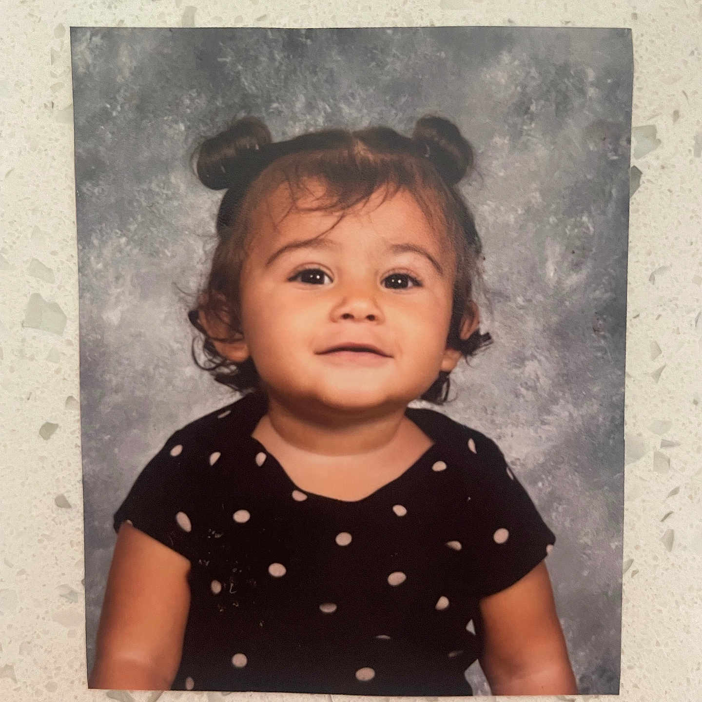 Aliyanna is registered to the contest to win money with this photo: arm, cheeks, child, clothing, countertop, cute, dress, eyes, hair_buns, indoor, person, photograph, polka_dot, portrait, printed_photo, smile, studio_backdrop, toddler, wall, young