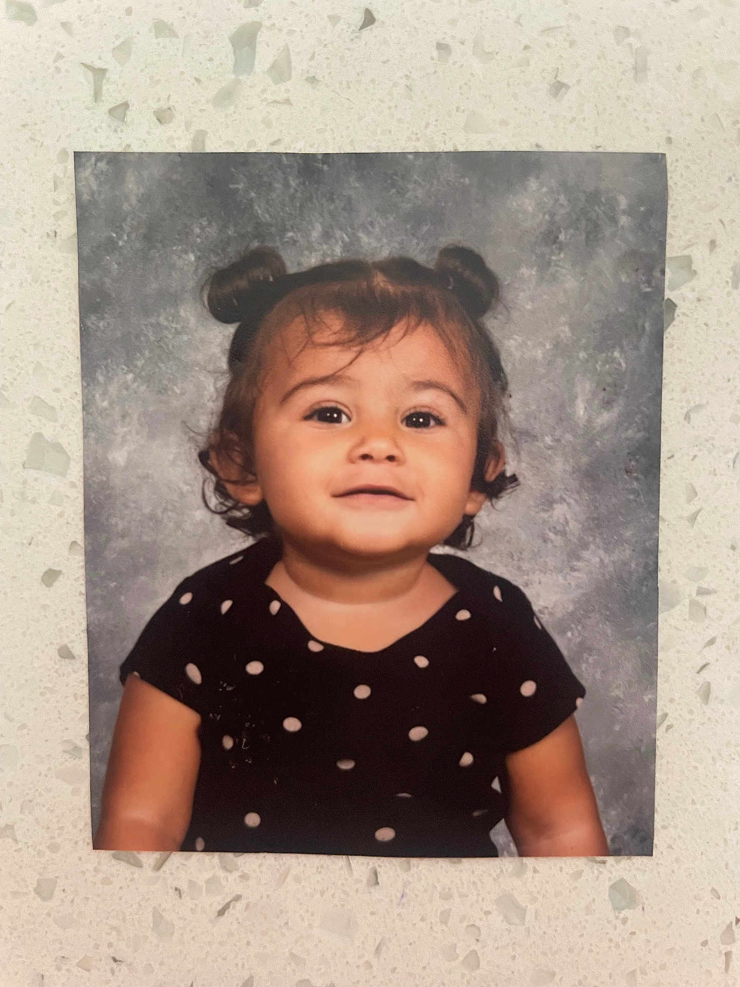 Aliyanna is registered to the contest to win money with this photo: child, toddler, portrait, polka_dot, dress, hair_buns, smile, eyes, cheeks, arm, studio_backdrop, printed_photo, countertop, wall, indoor, cute, young, person, photograph, clothing