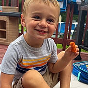 Asher is registered to the contest to win money with this photo: child, boy, smiling, snack, cracker, wooden_deck, porch, towels, railings, outdoor, summer, striped_shirt, khaki_shorts, barefoot, lunchbox, plastic_playset, portrait, happy, playtime, backyard