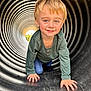 Asher joined the competition — help win amazing prizes! child, boy, toddler, playground, tunnel, crawling, smile, portrait, blond_hair, blue_eyes, concentric_rings, corrugated_tube, hands, jeans, green_shirt, outdoor, sunlight, play, happy, slide_surface