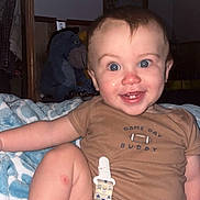 James joined the competition — help win amazing prizes! baby, child, infant, smiling, happy, sitting, bedroom, blanket, brown_clothing, stuffed_animal, elephant_toy, pacifier_clip, baby_gear, portrait, indoors, furniture, bed, patterned_blanket, blue_eyes, flash_photography