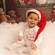 Josiah joined the competition — help win amazing prizes! baby, child, christmas, holiday, festive, santa_hat, pajamas, smiling, indoors, floor, wooden_floor, teddy_bear, gift, decorations, winter, snow, window, red, white, cute