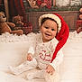 baby, child, christmas, holiday, festive, santa_hat, pajamas, smiling, indoors, floor, wooden_floor, teddy_bear, gift, decorations, winter, snow, window, red, white, cute