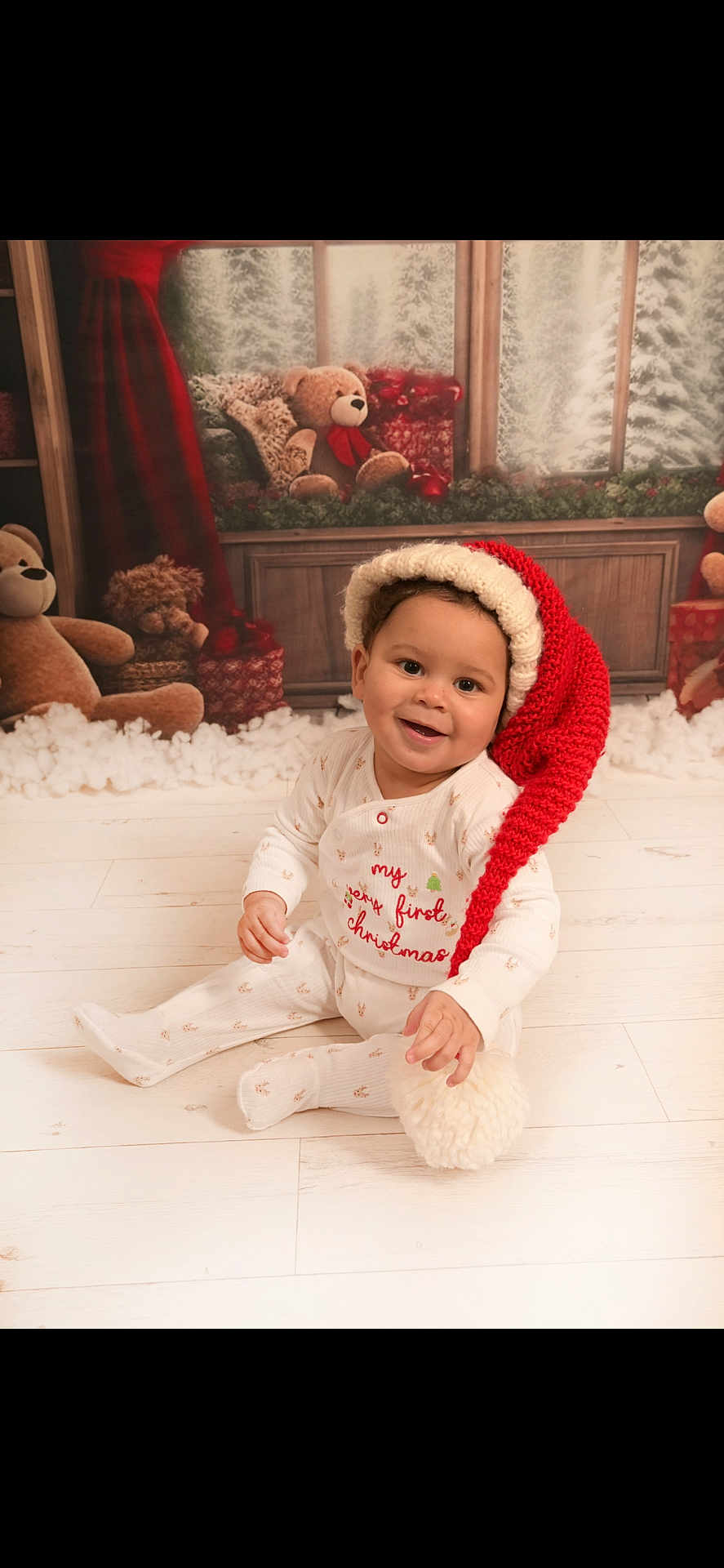 Josiah joined the competition — help win amazing prizes! baby, child, christmas, holiday, festive, santa_hat, pajamas, smiling, indoors, floor, wooden_floor, teddy_bear, gift, decorations, winter, snow, window, red, white, cute