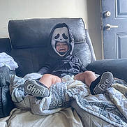 Chevy joined the competition — help win amazing prizes! toddler, child, costume, ghost_face, socks, smiling, armchair, blanket, indoor, door, happy, clothing, footwear, black_hoodie, fabric, home, cute, sitting, playful, portrait