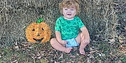 Chevy is registered to the contest to win money with this photo: toddler, child, pumpkin, hay_bales, fall_leaves, outdoor, porch, adults, skull_decoration, green_shirt, barefoot, grass, smiling, diaper, curly_hair, casual, daylight, house, plants, autumn