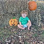 toddler, child, pumpkin, hay_bales, fall_leaves, outdoor, porch, adults, skull_decoration, green_shirt, barefoot, grass, smiling, diaper, curly_hair, casual, daylight, house, plants, autumn