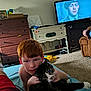 Boss is registered to the contest to win money with this photo: bed, black_and_white_cat, boy, carpet, carpeted_floor, cat, child, couch, cuddling, drawer, face, furniture, home, indoor, living_room, person, red_hair, shirtless, television, television_screen