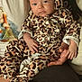 baby, infant, leopard_print, clothing, headband, person, hand, lap, couch, fabric, pattern, cute, portrait, young_child, indoor, skin, face, sitting, comfort, expression