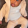 baby, child, infant, clothing, hoodie, sneakers, white_shoes, beige_pants, beige_hoodie, nike_logo, sitting, looking_away, curious, indoor, portrait, cute, young_child, person, face, feet