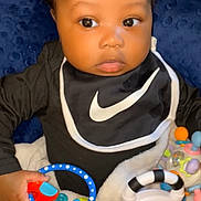 Dahari is registered to the contest to win money with this photo: baby, infant, toy, bib, black_clothing, blanket, cushion, curious, indoor, child, colorful_toys, closeup, cute, face, hand, sitting, portrait, young_child, soft_texture, playtime