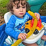 toddler, child, curly_hair, blue_clothing, toy, plastic_toy, yellow_tube, water_play, baby_seat, outdoor, grass, slide, backyard, greenery, summer, playtime, face, person, expression, sitting