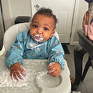 Stevie joined the competition — help win amazing prizes! baby, high_chair, messy, food, yogurt, bib, dinosaur_pattern, face, hands, tray, indoor, kitchen, door, table, bag, curious, child, sitting, clothing, floor