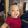Stevie joined the competition — help win amazing prizes! baby, child, smiling, tongue_out, striped_shirt, indoor, kitchen, cabinet, door, window, curtains, person, holding, happy, home, adult_hand, coffee_maker, clothing, face, living_room