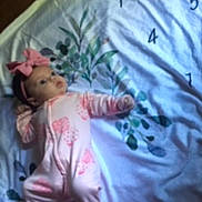 Violet is registered to the contest to win money with this photo: baby, infant, pink_onesie, headband, bow, milestone_blanket, floral_pattern, laying_down, curious_look, soft_lighting, cute, child, newborn, indoors, blanket, fabric, person, sleepwear, footed_pajamas, baby_toy