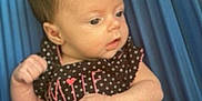 Violet is registered to the contest to win money with this photo: baby, infant, child, polka_dot, clothing, diaper, curtains, blue, sitting, portrait, face, skin, hair, fist, expression, indoors, cute, young, person, apparel