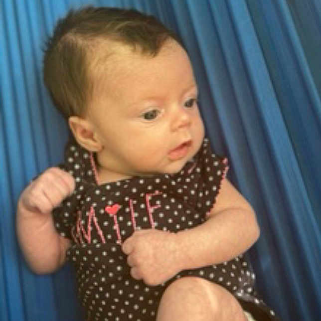 Violet is registered to the contest to win money with this photo: apparel, baby, blue, child, clothing, curtains, cute, diaper, expression, face, fist, hair, indoors, infant, person, polka_dot, portrait, sitting, skin, young