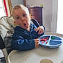 toddler, child, high_chair, blue_jacket, plate, food, indoor, table, expression, surprised, face, hand, furniture, window, cabinet, light, person, meal, cute, home
