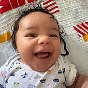 Zechariah joined the competition — help win amazing prizes! baby, smiling, happy, infant, face, portrait, clothing, onesie, patterned_clothing, lying_down, blanket, curly_hair, cute, child, person, indoor, closeup, skin, joy, expression