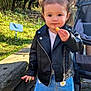 toddler, child, outdoor, park, leather_jacket, blue_skirt, daisy_print, white_shoes, pigtails, snack, stroller, sunny, grass, trees, sidewalk, curious, portrait, casual_clothing, daytime, young_child