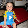 Caleb joined the competition — help win amazing prizes! child, toddler, smiling, sitting, bedroom, bed, bedding, pillow, air_conditioner, curtains, indoor, portrait, colorful_clothing, blue_outfit, yellow_outfit, barefoot, happy, home, candid, photograph