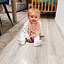 baby, child, infant, floor, bib, pink, toy, crib, chair, wooden_floor, home_interior, furniture, smiling, cute, sitting, white_clothes, happy, indoor, person, flooring
