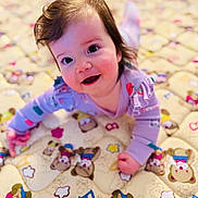 Adele is registered to the contest to win money with this photo: baby, child, smiling, crawling, purple_clothing, quilt, teddy_bear_pattern, indoor, cute, face, happy, infant, playful, young_child, person, soft_lighting, closeup, head, cheerful, colorful
