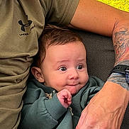 Sohan a rejoint le concours — aidez-le/la à gagner de superbes lots ! adult, arm, baby, background, child, closeup, curious, expression, face, green_clothing, hand, indoor, infant, person, seated, skin, sweatshirt, table, tattoo, watch