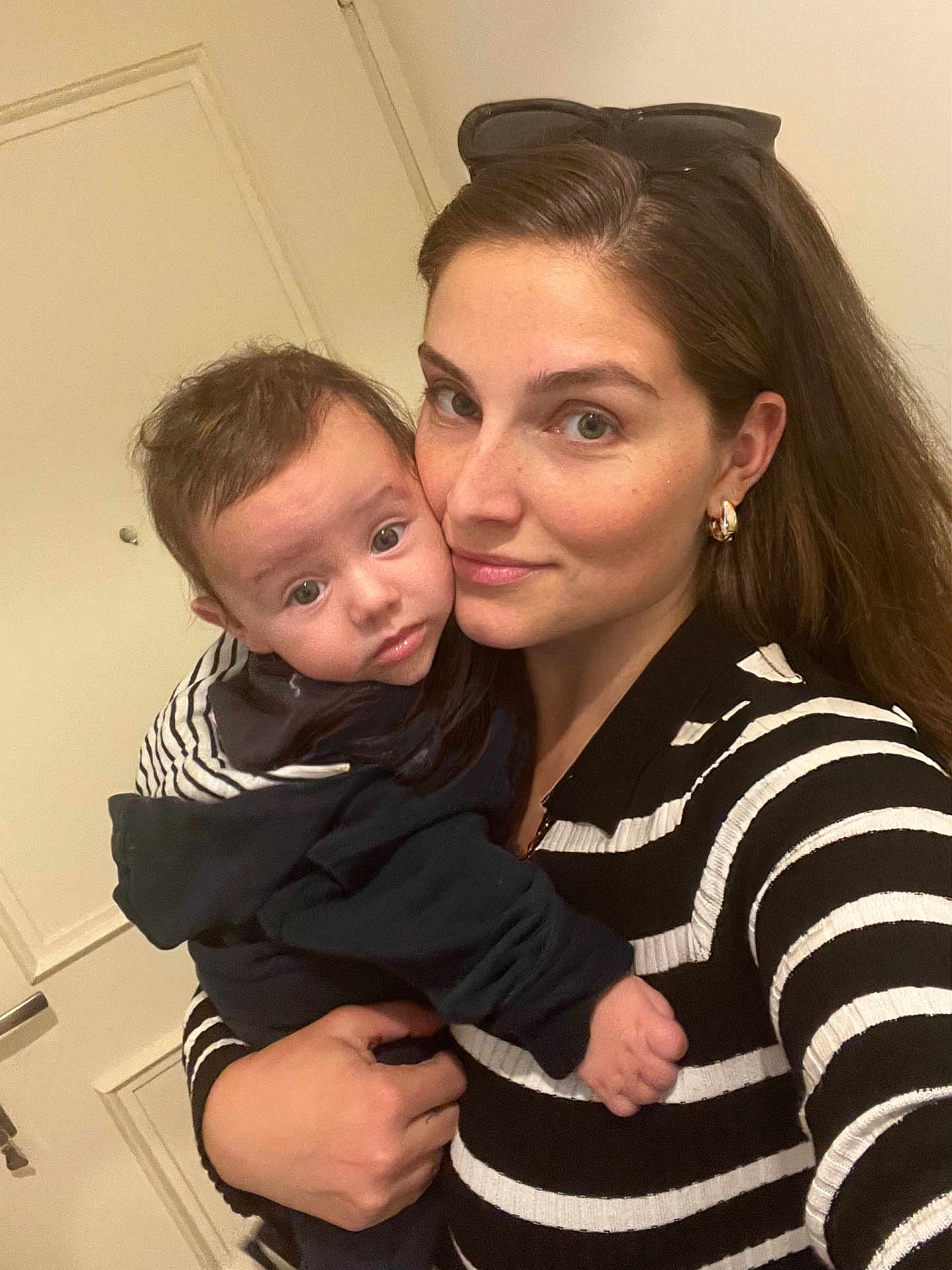 Sohan participe au concours pour gagner de l'argent avec cette photo : woman, baby, child, holding, indoor, striped_clothing, black_and_white, portrait, face, person, close_up, eyewear, gold_earrings, curly_hair, long_hair, casual_clothing, door, hand, soft_lighting, selfie
