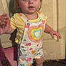 Ellie is registered to the contest to win money with this photo: apparel, baby, carpet, child, cute, door, expression, footwear, holding, holding_hand, indoor, overalls, person, portrait, rainbow_heart, standing, toddler, white_shoes, yellow_shirt, young_child