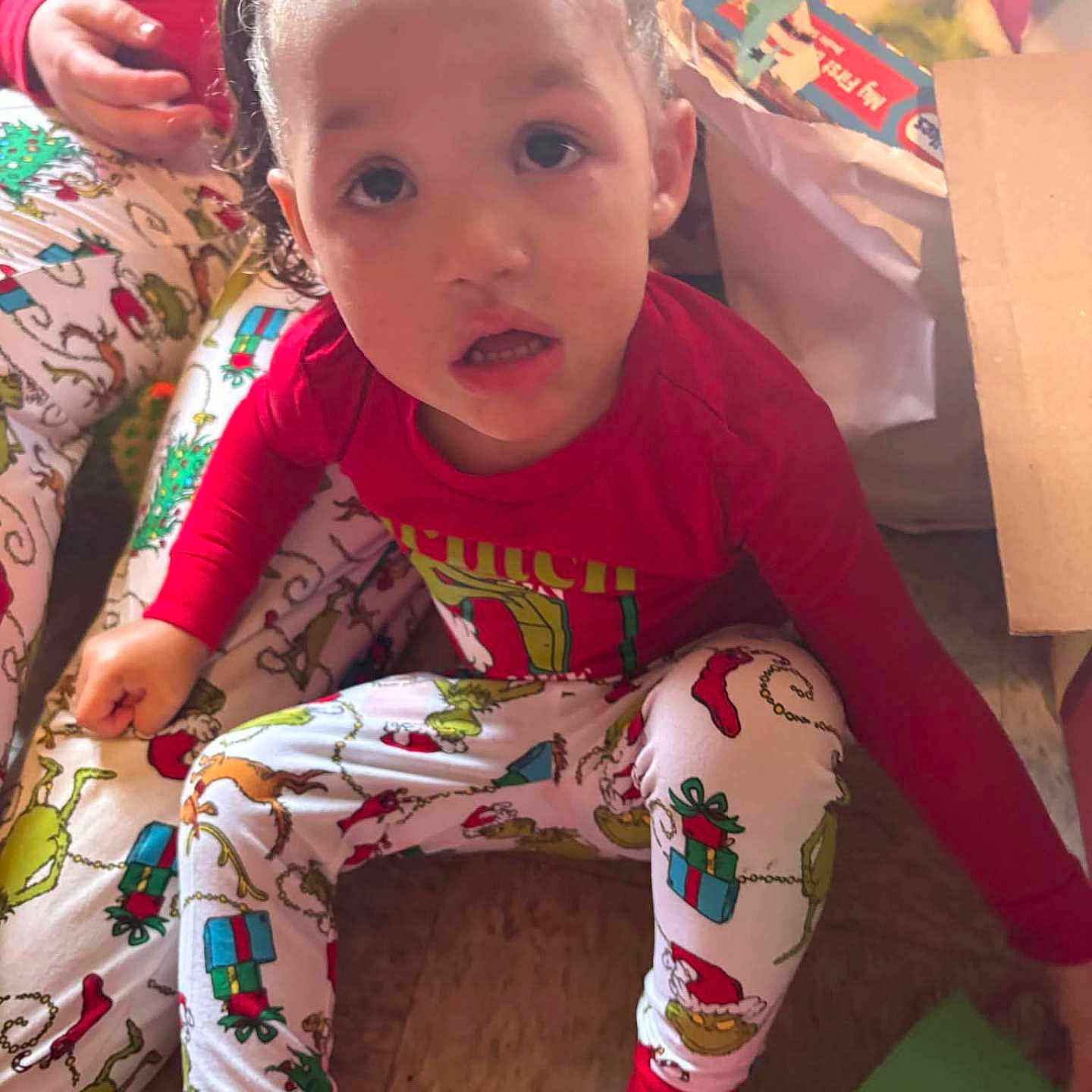 Maddisyn Wilkinson joined the competition — help win amazing prizes! child, pajamas, holiday, christmas, grinch, gift, wrapping_paper, box, floor, sitting, red_shirt, patterned_clothing, indoor, person, cute, festive, curious, young_child, holiday_decor, casual