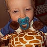child, toddler, baby, pacifier, plush_toy, giraffe, stuffed_animal, portrait, close_up, smiling, blue_clothing, red_hair, indoor, nursery, toy, cuddly, cozy, face, sitting, photography