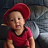 armchair, baby, blue_gray_furniture, casual, child, clothing, comfortable, curious, expression, face, headwear, home, indoor, infant, person, portrait, red_cap, red_shirt, sitting, young_child