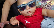 Zeremiah is registered to the contest to win money with this photo: adult_arm, baby, blanket, casual, casual_clothing, child, closeup, cute, fashion, hand, holding, indoor, person, portrait, red_shirt, relaxed, seat, serious_expression, sunglasses, toddler