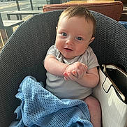 Hunter is registered to the contest to win money with this photo: baby, child, smile, blue_blanket, knitted_blanket, chair, indoor, purse, white_purse, person, happy, face, hands, clothing, window, daylight, seated, cute, infant, portrait
