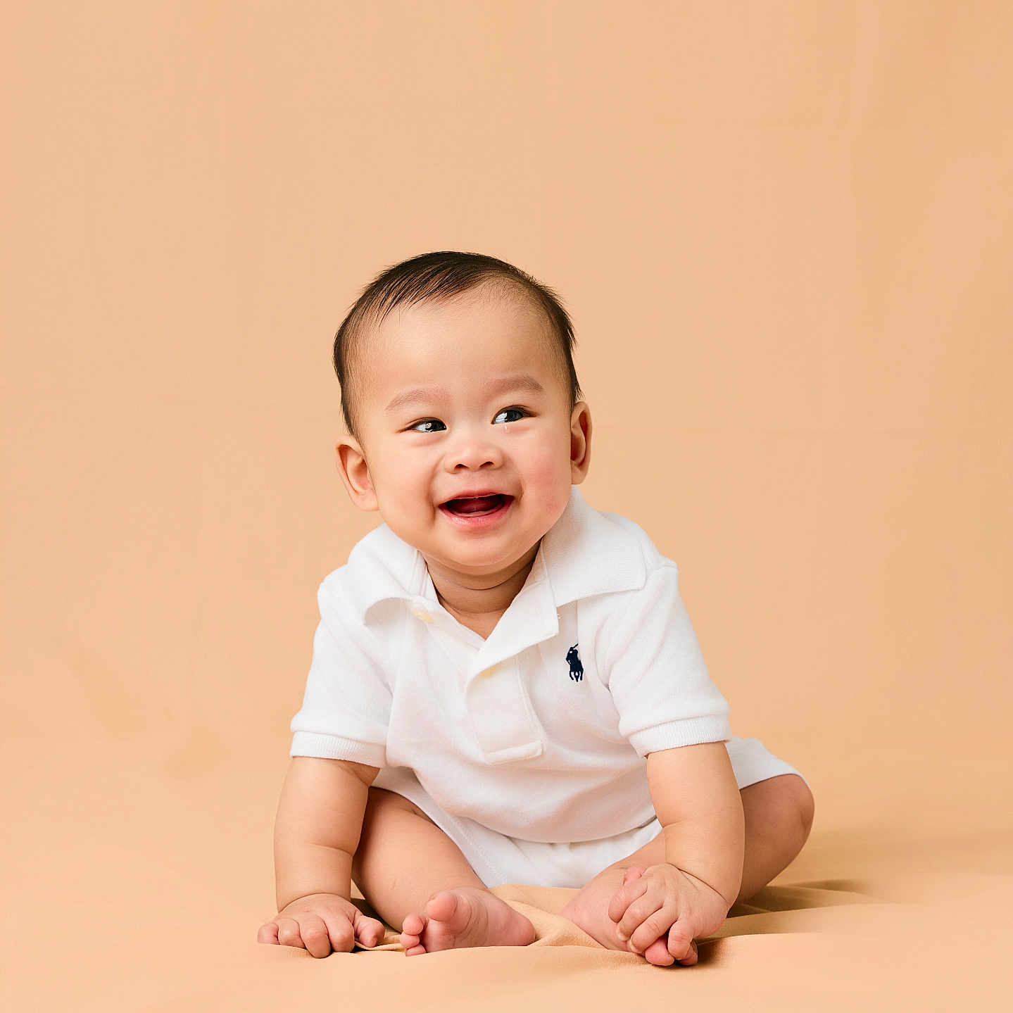 Rei is registered to the contest to win money with this photo: baby, beige_background, child, cute, expression, face, feet, hands, happy, indoors, infant, one_person, polo_shirt, portrait, sitting, skin, smiling, studio, white_clothing, young